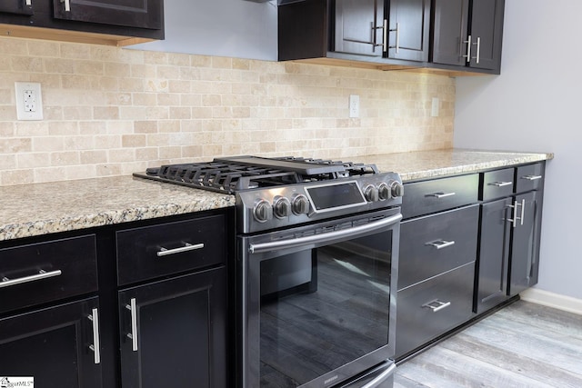 kitchen with tasteful backsplash, stainless steel gas stove, dark cabinets, light wood-type flooring, and baseboards