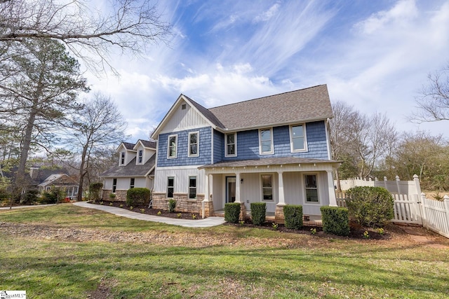 craftsman-style house featuring stone siding, a porch, fence, and a front lawn