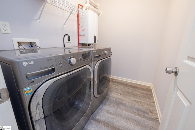 clothes washing area featuring tankless water heater, laundry area, separate washer and dryer, wood finished floors, and baseboards