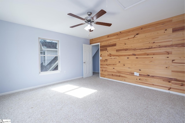 carpeted spare room featuring ceiling fan, wood walls, attic access, and baseboards