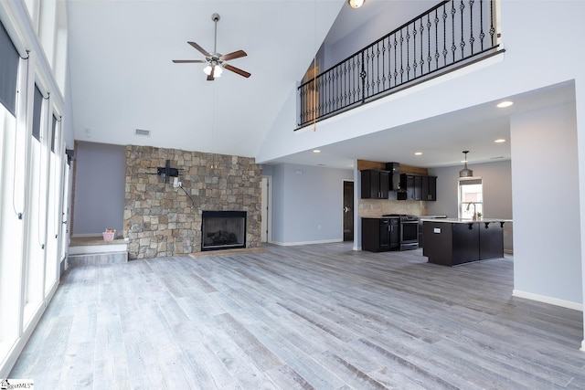 unfurnished living room featuring ceiling fan, a stone fireplace, a sink, visible vents, and light wood-type flooring