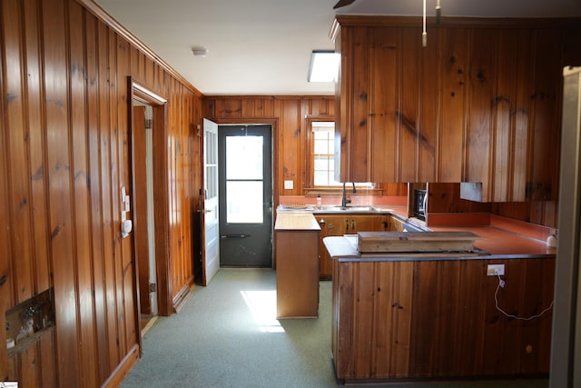 kitchen featuring a center island, brown cabinetry, a sink, wooden walls, and a peninsula