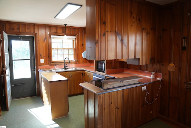 kitchen with wooden walls, brown cabinetry, decorative light fixtures, a peninsula, and a sink