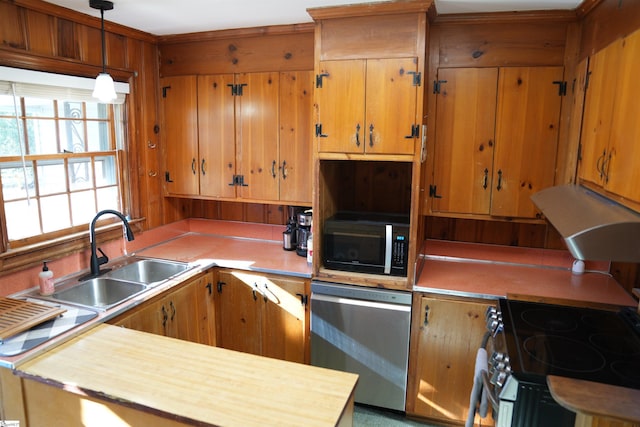 kitchen featuring wooden walls, stainless steel appliances, a sink, light countertops, and pendant lighting