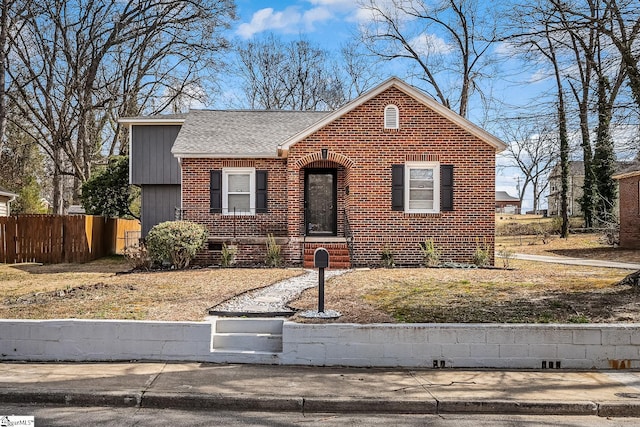 view of front facade with brick siding, fence, and roof with shingles