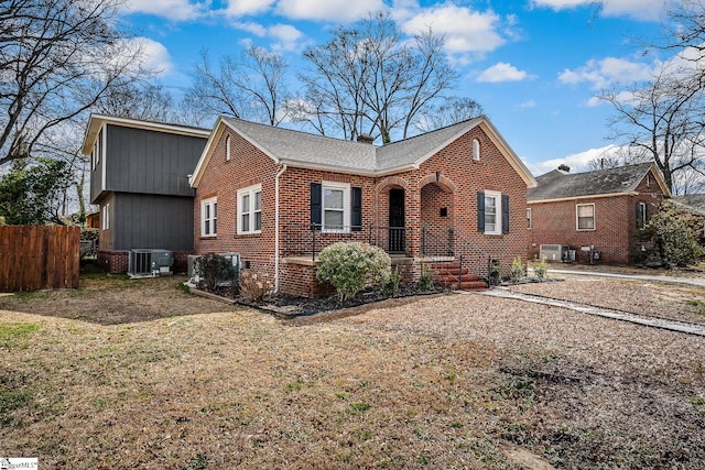 view of front of house with brick siding, a chimney, central AC unit, and fence