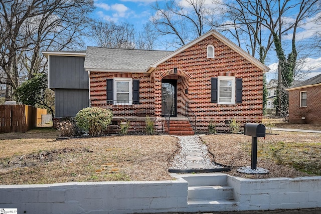 view of front facade featuring brick siding, roof with shingles, and fence