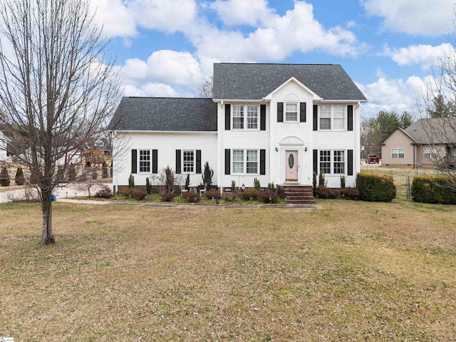 colonial inspired home with a front lawn, roof with shingles, and fence