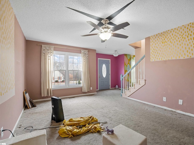 carpeted living area with stairs, ceiling fan, a textured ceiling, and baseboards