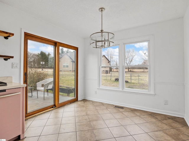 unfurnished dining area featuring a chandelier, a textured ceiling, plenty of natural light, and visible vents