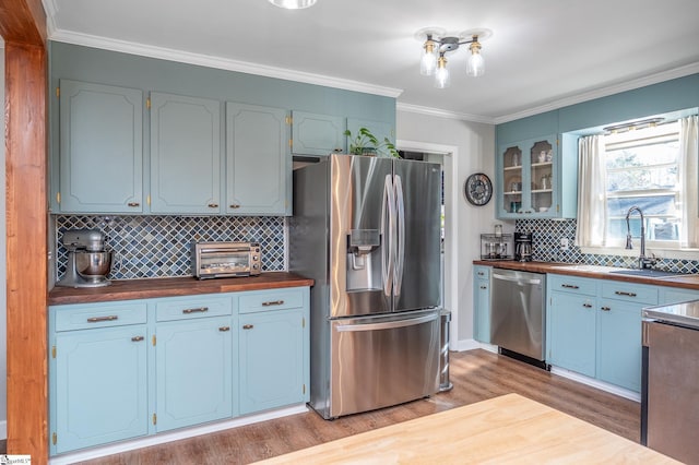 kitchen featuring a toaster, stainless steel appliances, light wood-style flooring, glass insert cabinets, and ornamental molding