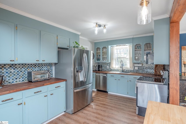 kitchen with butcher block counters, appliances with stainless steel finishes, ornamental molding, light wood-style floors, and a sink