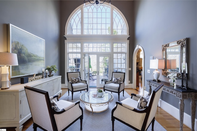 living room featuring french doors, light wood-style floors, a towering ceiling, and a healthy amount of sunlight