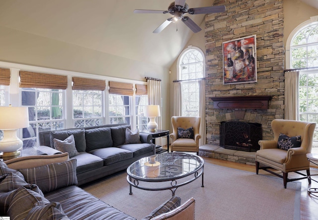 living area featuring high vaulted ceiling, a ceiling fan, a stone fireplace, and wood finished floors