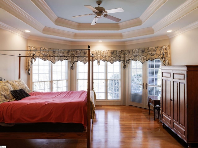 bedroom featuring ornamental molding, access to outside, a tray ceiling, and wood finished floors