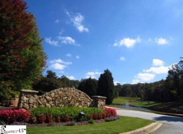 community sign featuring a forest view and a yard