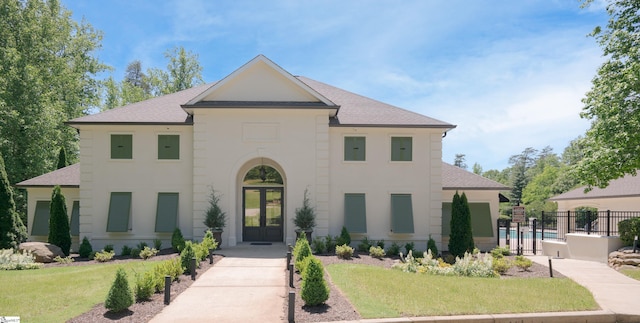 view of front of house featuring roof with shingles, fence, french doors, a front lawn, and stucco siding