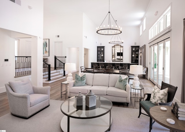 living area featuring a chandelier, visible vents, a towering ceiling, light wood-style floors, and stairway