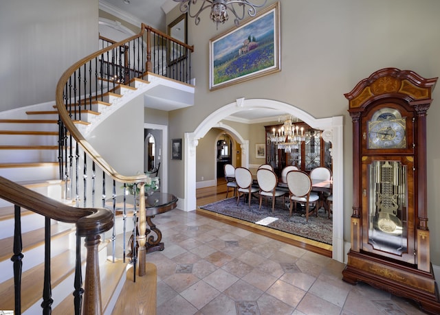 foyer with a chandelier, arched walkways, a high ceiling, baseboards, and ornamental molding