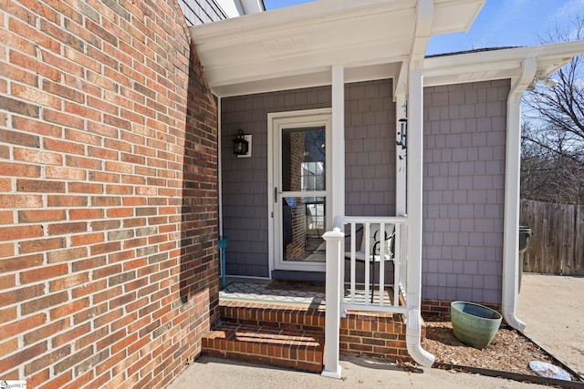 doorway to property with covered porch, brick siding, and fence