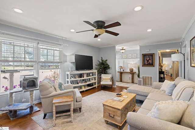 living area featuring visible vents, wood finished floors, a wood stove, crown molding, and recessed lighting