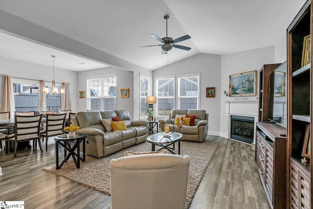 living area featuring vaulted ceiling, ceiling fan with notable chandelier, a fireplace, and wood finished floors