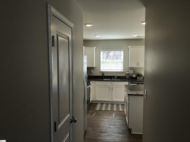 kitchen with stainless steel appliances, a sink, white cabinets, dark wood-style floors, and dark countertops