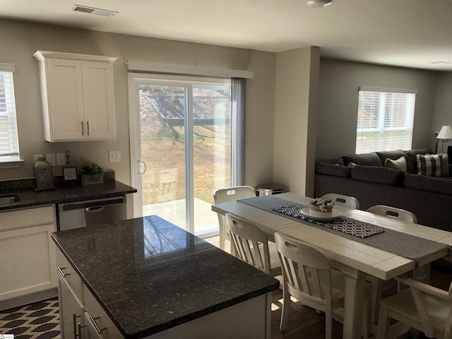 kitchen with a kitchen island, visible vents, white cabinets, stainless steel dishwasher, and dark stone countertops