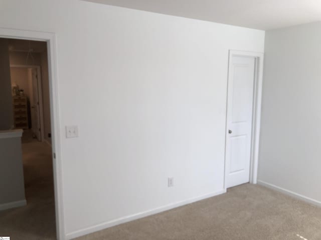 spare room featuring light carpet and baseboards