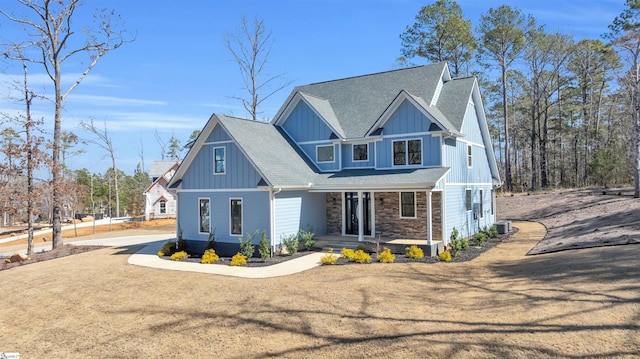 view of front of house with board and batten siding, stone siding, a shingled roof, and a front lawn