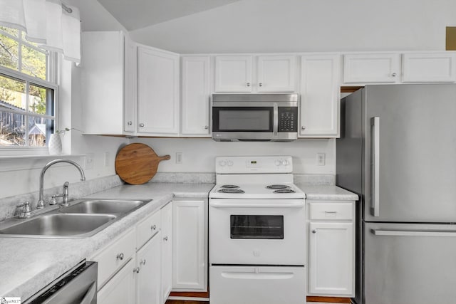 kitchen featuring white cabinets, vaulted ceiling, stainless steel appliances, and a sink