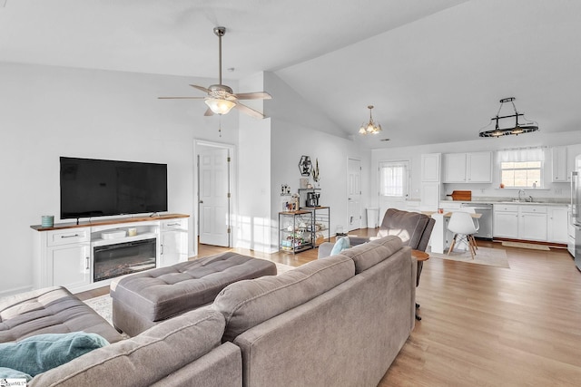 living area featuring lofted ceiling, ceiling fan, light wood-type flooring, and a glass covered fireplace