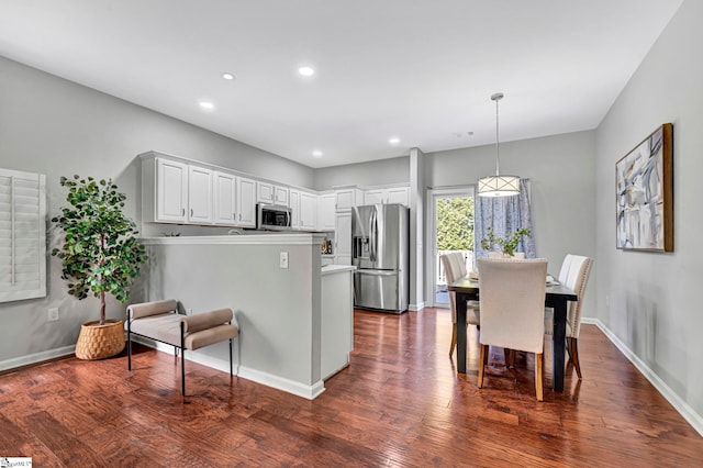 kitchen with a peninsula, white cabinetry, stainless steel appliances, and dark wood-type flooring