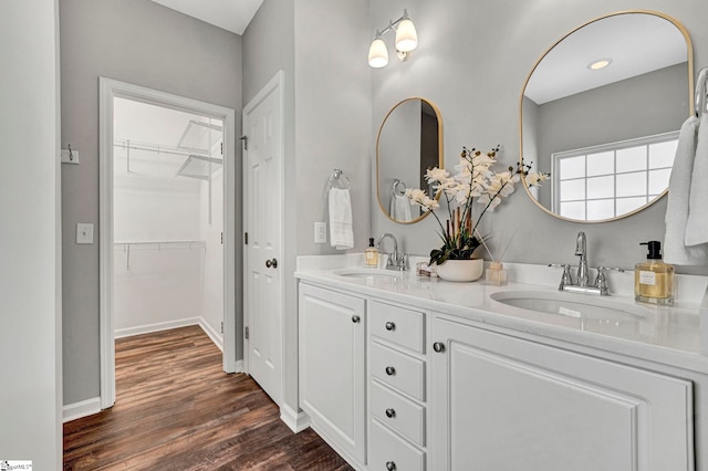 full bathroom with double vanity, wood finished floors, a sink, and baseboards