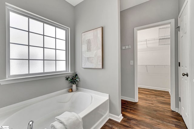 full bathroom with wood finished floors, a spacious closet, baseboards, and a bath