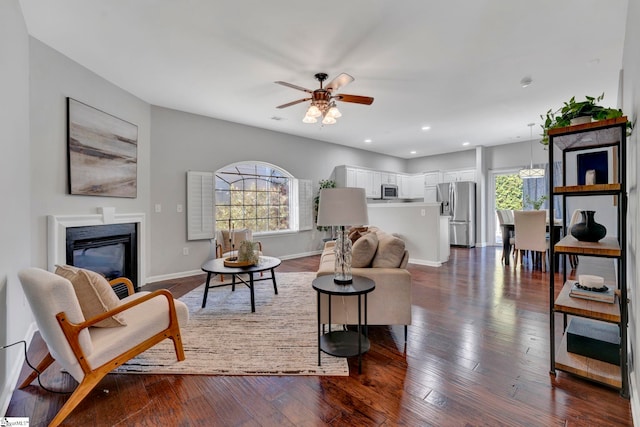 living area with a glass covered fireplace, plenty of natural light, dark wood finished floors, and baseboards