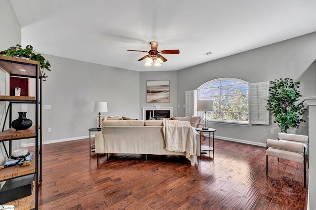 living room featuring a ceiling fan, dark wood-style flooring, a fireplace, and baseboards