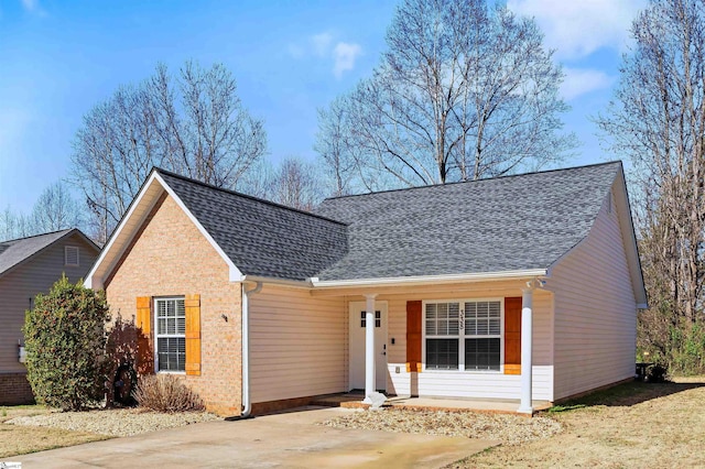 view of front of home with covered porch, roof with shingles, and brick siding