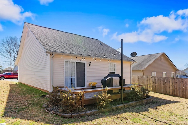 back of property with a shingled roof, a yard, fence, and a deck