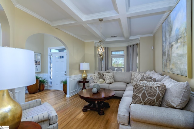 living area featuring wainscoting, light wood-style flooring, beam ceiling, and visible vents