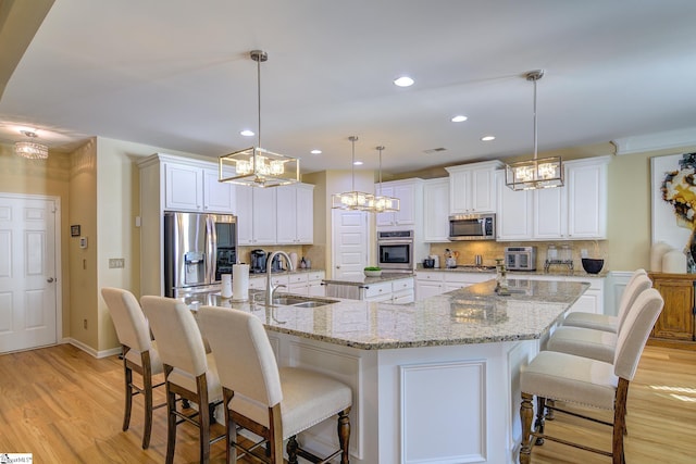 kitchen with a large island, decorative backsplash, appliances with stainless steel finishes, a sink, and light wood-type flooring