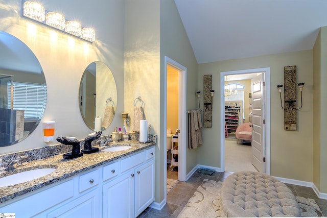 bathroom featuring lofted ceiling, a walk in closet, a sink, and double vanity