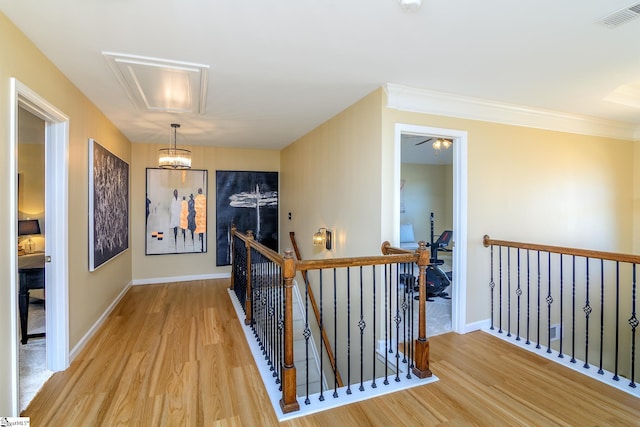 hallway featuring light wood-type flooring, baseboards, visible vents, and an upstairs landing