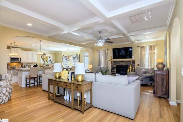 living area featuring arched walkways, a stone fireplace, light wood finished floors, and visible vents