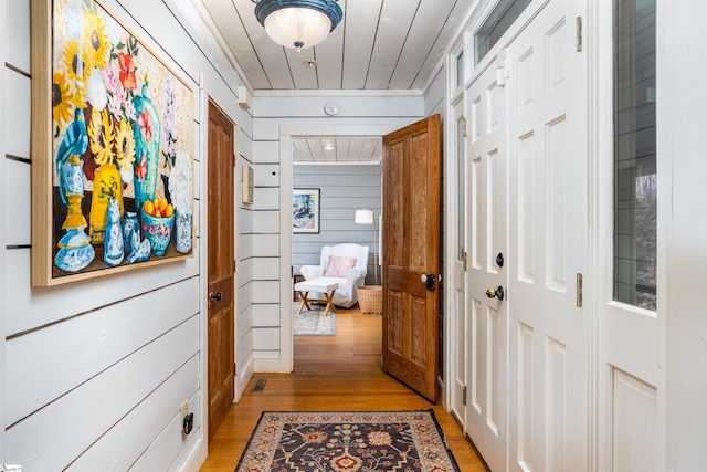 hall with light wood-type flooring, wooden ceiling, and wooden walls