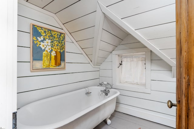 full bath with vaulted ceiling, wood walls, and a freestanding tub