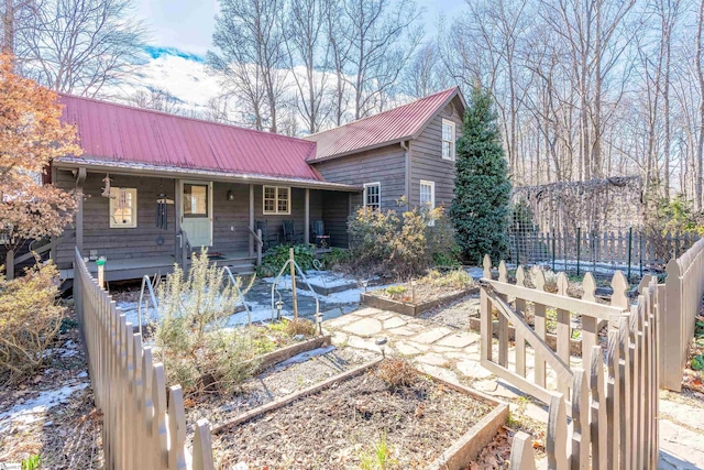 view of front of home featuring a porch, a garden, metal roof, and fence