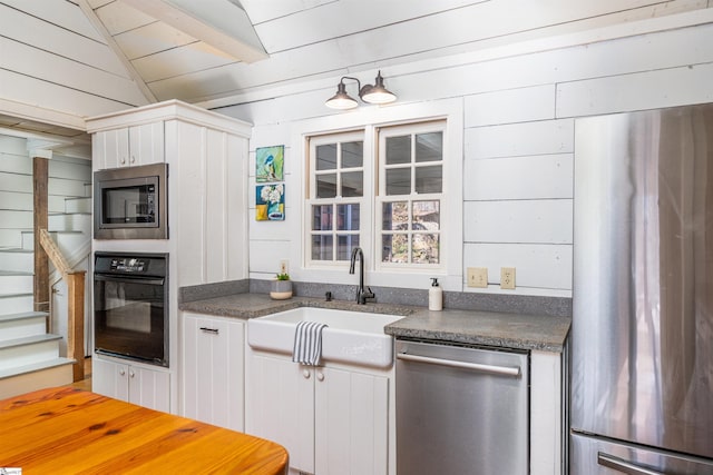 kitchen featuring stainless steel appliances, dark countertops, vaulted ceiling, a sink, and wooden walls