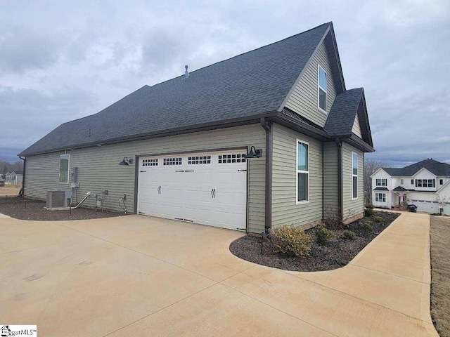 view of home's exterior with cooling unit, a shingled roof, a garage, and concrete driveway