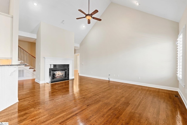 unfurnished living room with visible vents, baseboards, a tile fireplace, light wood-style floors, and high vaulted ceiling